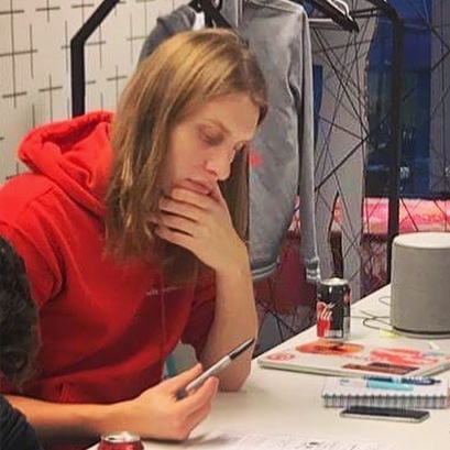 A person in a red hoodie sits at a table looking at a piece of paper while holding a pen