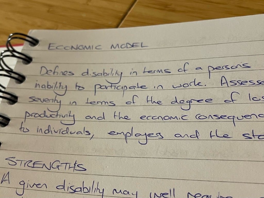 
Spiral bound notebook open to a page titled 'Economic model'.
Below the title, handwritten text as follows.
Defines disability in terms of a persons inability to participate in work.
Assesses severity in terms of the degree of lost productivity and the economic consequences to individuals, employers and the state.