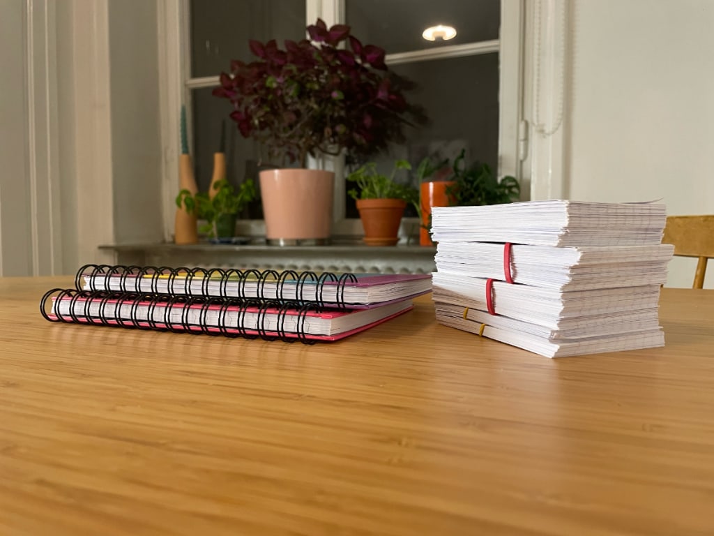 Two A5 spiral-bound notebooks on a wooden table next to a stack of flash cards about 15cm high. 